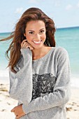 A young brunette woman by the sea wearing a grey sweatshirt