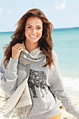 Junge, brünette Frau im grauen Sweatshirt mit Schal am Meer
