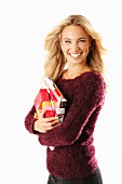 A young blonde woman holding presents and wearing a burgundy knitted jumper