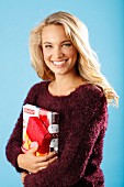 A young blonde woman holding presents and wearing a burgundy knitted jumper
