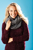 A young blonde woman wearing a burgundy knitted jumper and a grey scarf