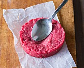 A raw hamburger being squashed with a spoon