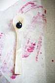 A red grape on a mother-of-pearl spoon with grape juice stains on a piece of paper
