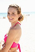 A young blonde woman on a beach wearing a pink bikini top