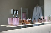 A toothbrush in a pink vintage ceramic cup along with perfume bottles on an illuminated glass shelf