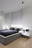 Minimalistisches Schlafzimmer mit Boxspringbett, schwarz-weiße Bettwäsche, seitlich an Wand schwebende Nachttischablage