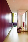 Flat-fronted purple cupboards, colourful waste-paper basket and floor-to-ceiling mirror on wall of modern hallway