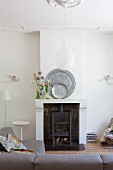 Pewter plates and wild flowers on mantelpiece; teardrop-shaped pendant lamp above sofa