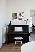 Pictures, letter K and framed butterflies on wall above piano with cat ornament and flowers on top
