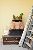 Vintage-style still-life arrangement on tray and rabbit ornament on stack of crates and suitcases next to carved wooden pillar and old ladder