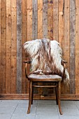 Antique bentwood chairs with sheepskin blanket against board wall