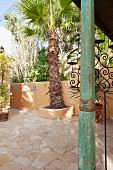 Wooden column with distressed green paint on Mediterranean terrace with palm trees
