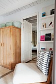 Chair with patterned scatter cushion in front of bookcase and simple wooden cupboard in Mediterranean bedroom