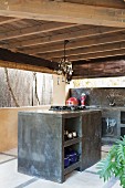 Outdoor kitchen with wooden ceiling, marbled concrete counters and glass lamp above hob on free-standing block