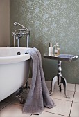 Vintage, clawfoot bathtub next to postmodern, silver-coated side table against wall with rolled paint pattern