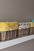 Detail of several baskets lined with patterned fabrics on white shelf on pale grey wall