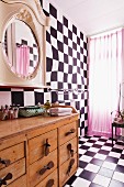 Chequered floor and wall, pink curtain on window and rustic, wooden chest of drawers