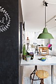 Pendant lamp with green metal lampshade above breakfast counter; woman in background next to dining area in open-plan interior