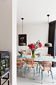 Flowers on dining table and wooden chairs with metal frames below two pendant lamps with metal lampshades