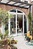 View from garden onto gravel terrace adjoining house with arched terrace doors and windows in brick facade