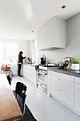 White kitchen counter along entire wall, extractor hood, dining area and woman in background