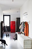 Simple trunk bench made of white-painted wood below coat rack; scooters and red, 50s fridge in background next to front door