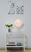 Pictures above lamp and vase of flowers on table on castors