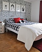 Schlafzimmer mit schwarz-weissen Bildern an Tapetenwand mit Paisleymuster und Doppelbett mit kariertem Bezug
