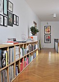 Gallery of pictures above books and records in sideboard compartments running along corridor; herringbone parquet floor