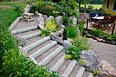 Terraced, gravel steps supported by boulders and with wooden edges in front of seating area on wooden decking