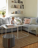 Toddler sitting on grey sofa in comfortable living room with books on floating shelves