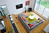 View from gallery down onto grey sofa combination with colourful scatter cushions and green rug surrounded by pale wooden surfaces
