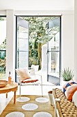 Bench with sisal seat and white chair on sisal rug with polka-dots; open door with view into garden in background