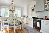 Square dining table and chairs below brass lamp and woven rugs in spacious, white, Scandinavian, country-house kitchen