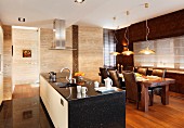 Free-standing kitchen counter clad in black stone and tasteful dining area with leather-covered chairs below modern pendant lamps