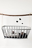 Hedgehog toy and knitted ball in dolls' crib hung from wooden pole; black paper leaf silhouettes on wall