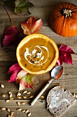 Autumnal pumpkin soup served in a hollowed out pumpkin with sour cream and pumpkin seeds