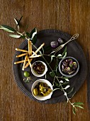 Olives, purple Brussels, bread sticks and an olive branch on a black plate