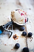 Blueberry ice cream in an ice cream scoop on a wooden surface with individual blueberries