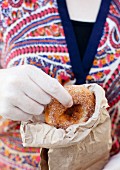 A woman taking a cinnamon sugar doughnut from a paper bag
