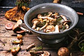 Fresh wild mushrooms with an old bowl filled with water on a wooden table