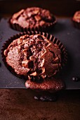 Dark chocolate muffins in a baking tin with the mixture spilling over the edge
