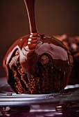 Melted chocolate being poured over a dark chocolate muffin