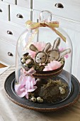 Easter arrangement under glass cover with hand-sewn Easter bunnies, moss and quails' eggs on cake stand