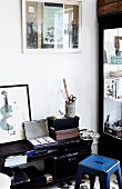 Storage boxes and drawing utensils on black, half-height shelves and blue, retro metal stool
