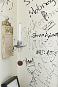 Scribbles and drawings on section of white wall and white candle in candle sconce