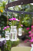 Glasgefäß mit Blumen am Haken im Garten