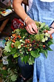 Woman tying wreath of rosehips, acorns, hops & chestnuts