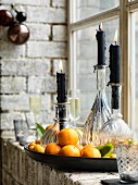 Black candles in round glass bottles standing in dish amongst tangerines