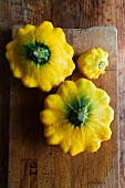 Three yellow patty pan squash on a chopping board (seen from above)